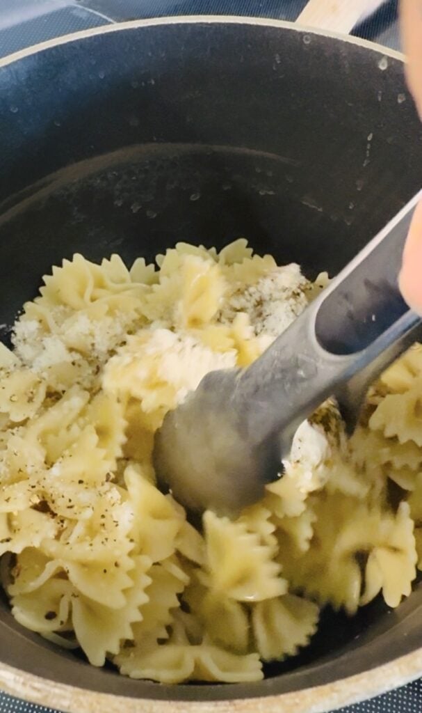 tossing the cooked pasta with seasonings